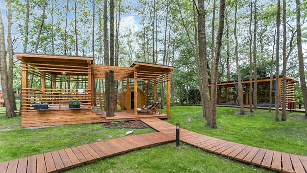 Une cabane en bois dotée d’une terrasse et d’une fenêtre ronde, entourée d’une forêt.