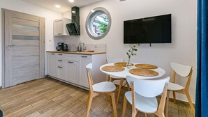 A modern kitchen with white cabinets, a round dining table with woven placemats, and a flat-screen TV mounted on the wall.
