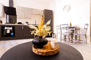 A modern kitchen with dark cabinets, a black vase with dried flowers, and a dining table with chairs. - City Getaway: Cosy 1Bed Apt in Hull Centre (Hull)