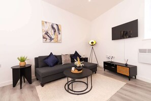 A modern living room with a black sofa, a round coffee table, a side table, a floor lamp, and a black TV stand. - City Getaway: Cosy 1Bed Apt in Hull Centre (Hull)