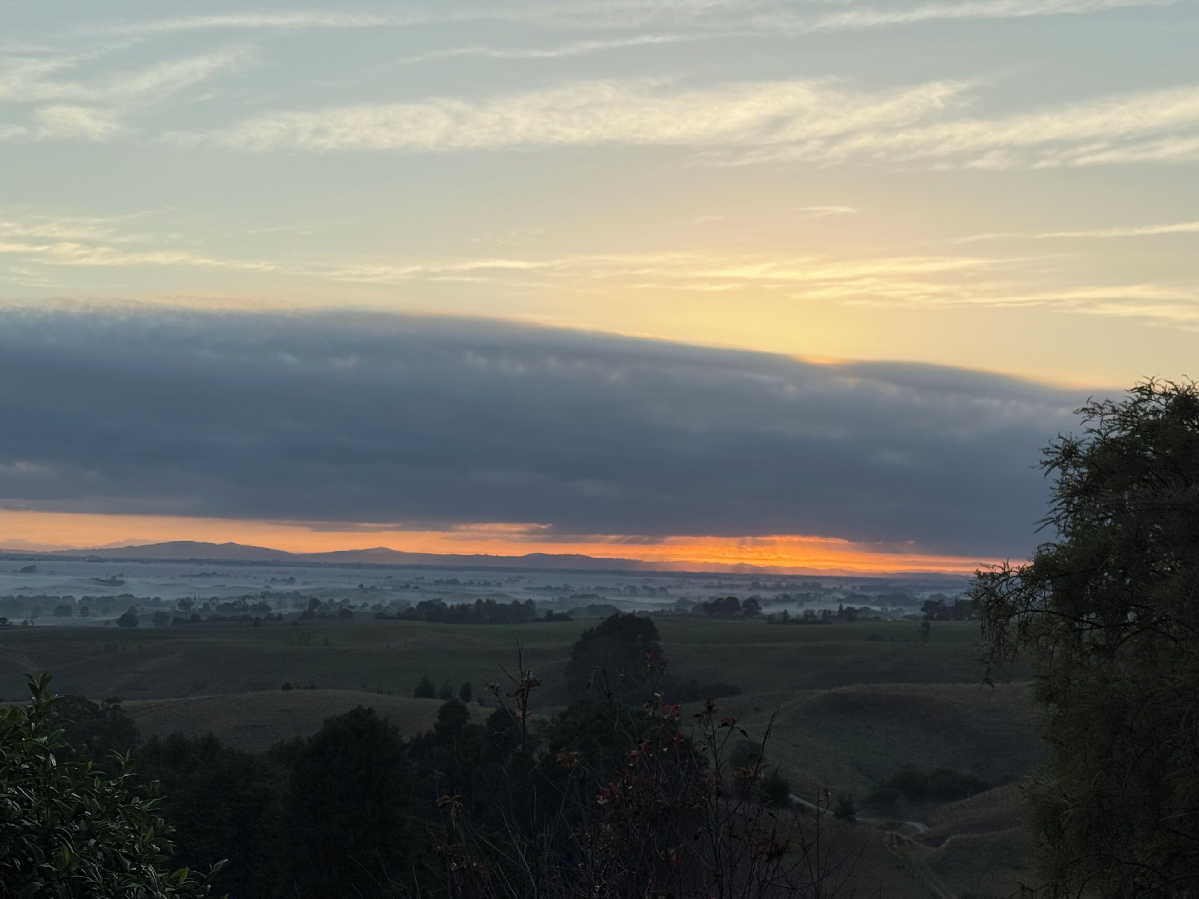 Un paysage de collines douces baigné par les couleurs d’un coucher de soleil.