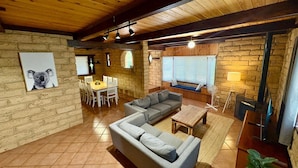 A cozy living room with a sofa, coffee table, and dining area with chairs. There is a fireplace and a window with blinds. - Timber Tides Retreat (Geographe)