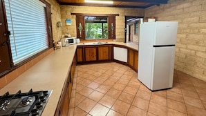 A kitchen with a gas stove, white refrigerator, wooden cabinets, and a window with blinds. - Timber Tides Retreat (Geographe)