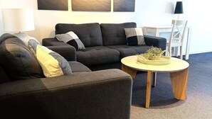 Moderni olohuone, jossa on tummanharmaa sohvaryhmä, pyöreä puinen sohvapöytä ja suuri abstrakti taulu seinällä.