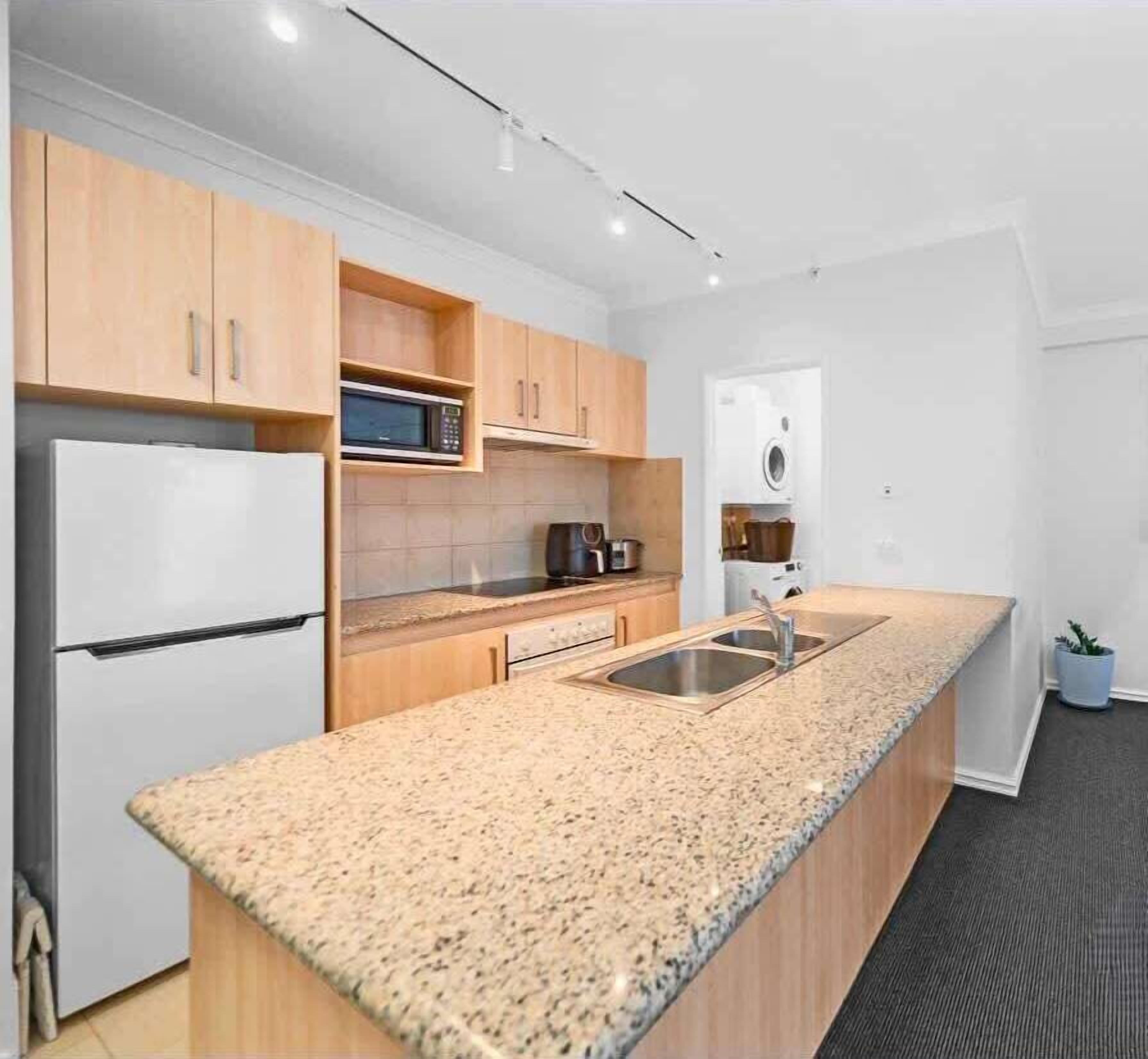 A modern kitchen with wooden cabinets, a granite countertop, a built-in microwave, and a sink.