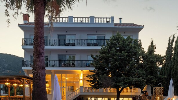 A swimming pool with blue lighting, a palm tree, and a building with balconies and outdoor seating.