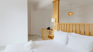 A hotel room with a wooden headboard, a bed with white linens, a bedside table with a lamp, and a view of the hallway.
