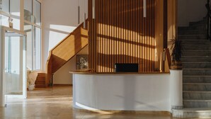 A reception area with a wooden reception desk, a staircase, and a large window allowing natural light.