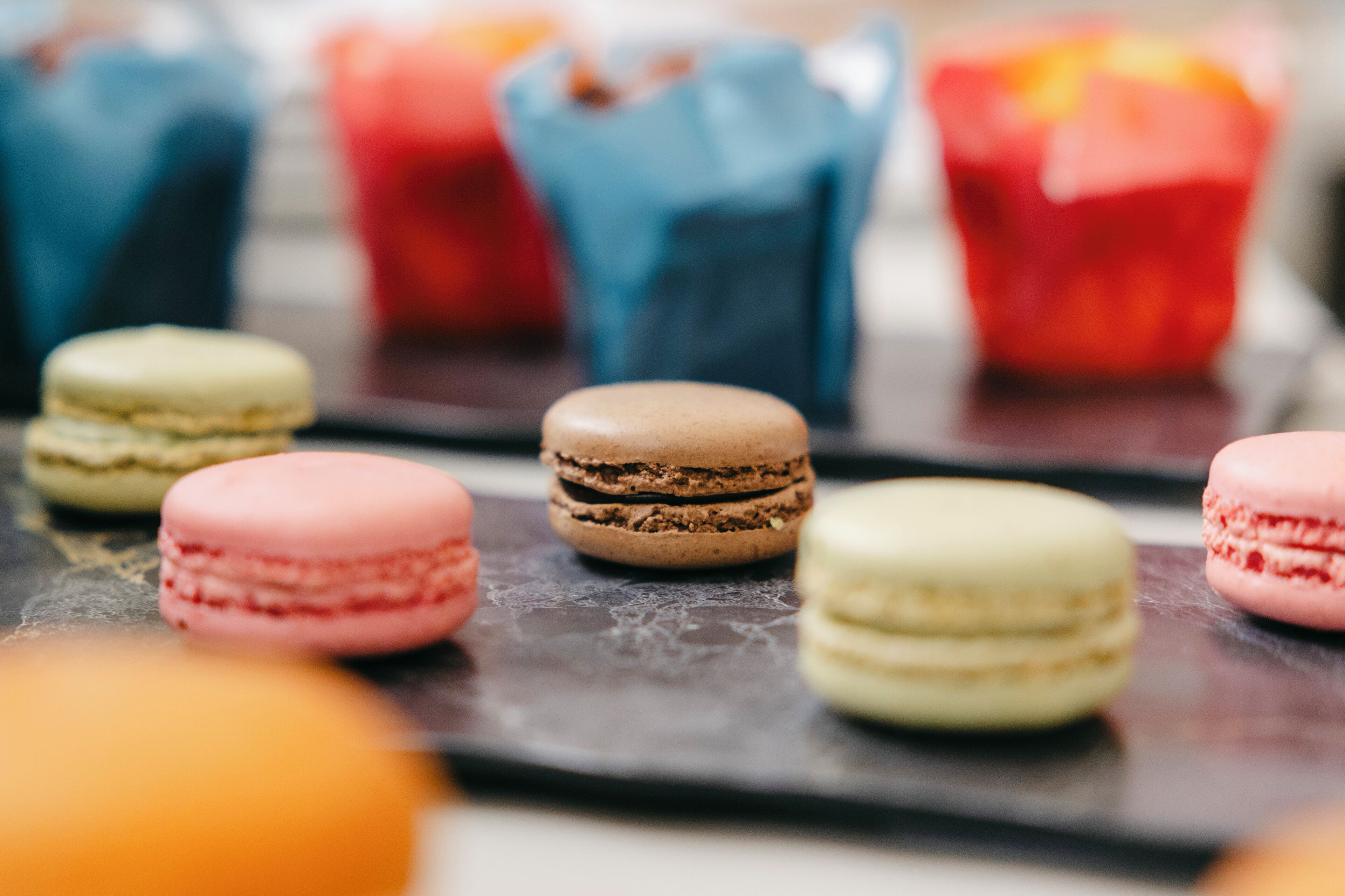 Macarons op een leistenen schaal met kleurrijke papieren bekertjes op de achtergrond.