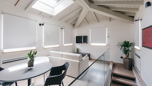 A modern living room with a high ceiling, skylights, a sofa, a dining table, and a staircase. - Villa Turco Berti Luxury Apartments&SPA (Caldiero)