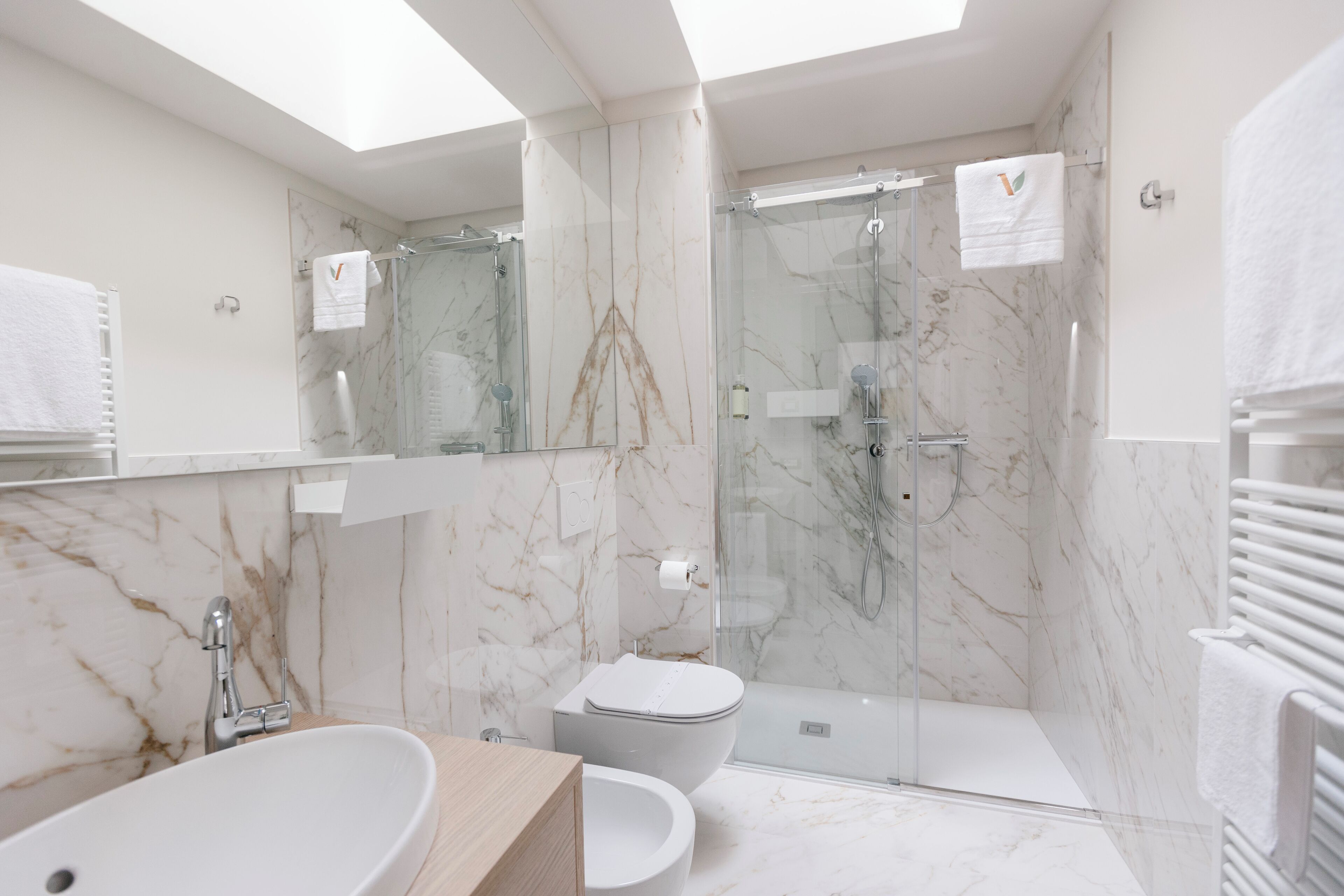Un baño moderno con suelo de mármol, una bañera independiente, un inodoro y una zona de ducha con mampara de cristal.