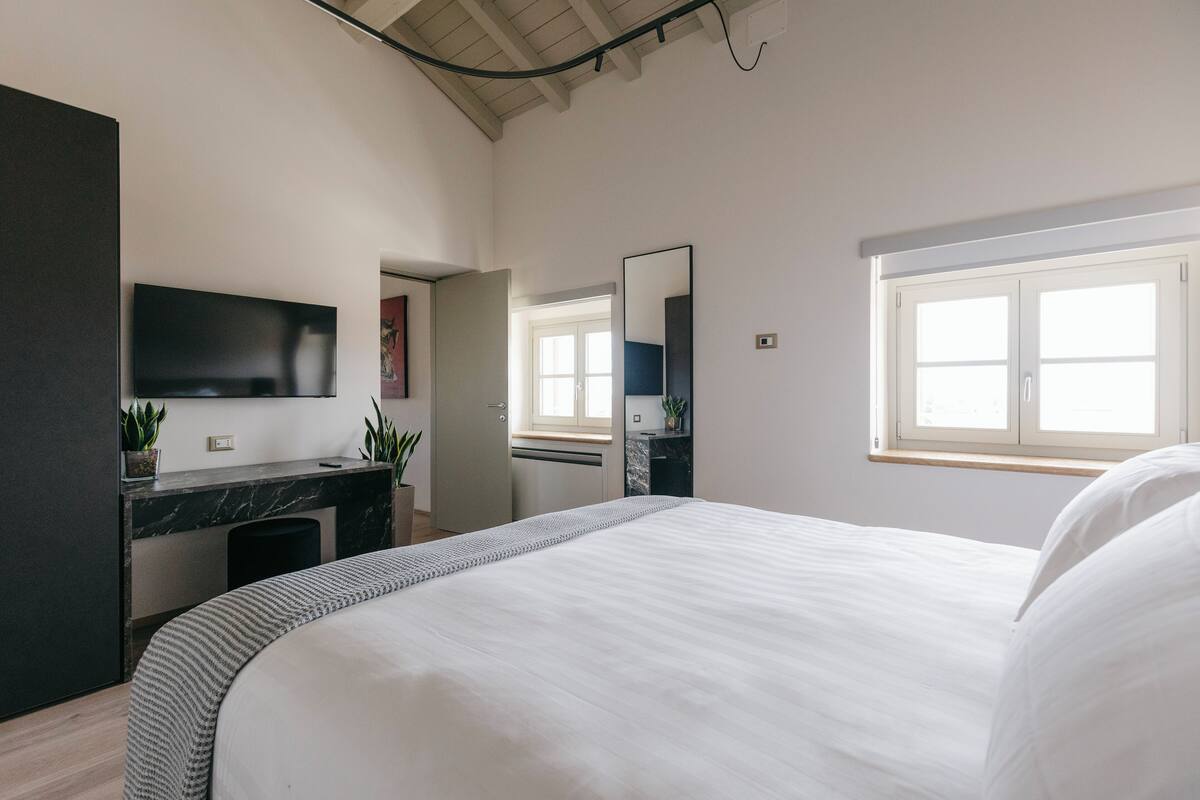 Ein Schlafzimmer mit einem Bett, einem Fernseher, einem Schreibtisch und einem Fenster.