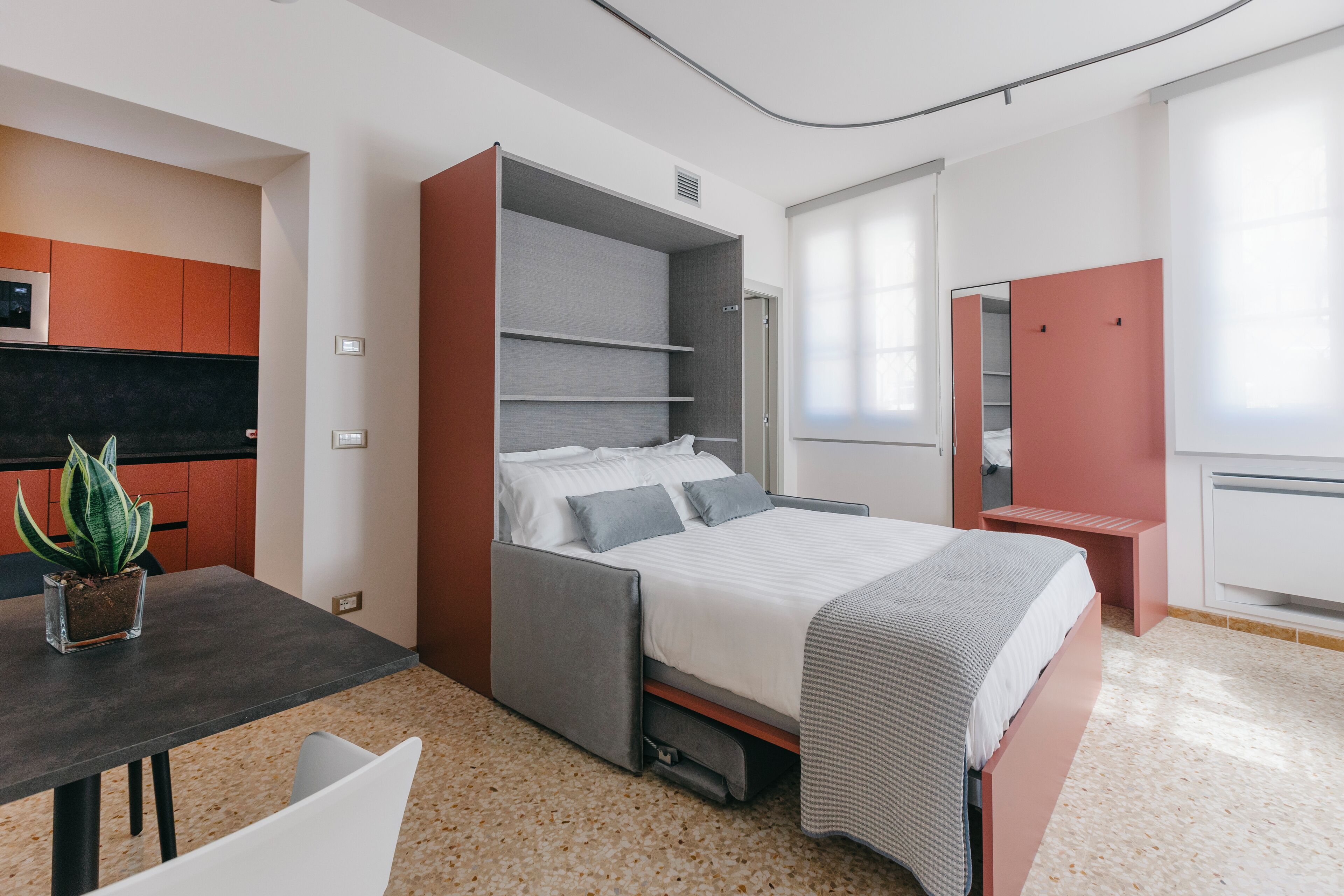 Ein modernes Schlafzimmer mit Bett, Schreibtisch und Stuhl. Auf dem Schreibtisch steht ein Blumentopf.