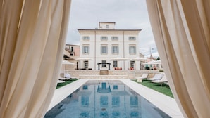 A pool area with a view of a large building, lounge chairs, and umbrellas. - Villa Turco Berti Luxury Apartments&SPA (Caldiero)
