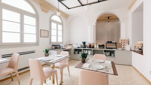 A modern dining area with a high ceiling, large windows, and a kitchen in the background. - Villa Turco Berti Luxury Apartments&SPA (Caldiero)