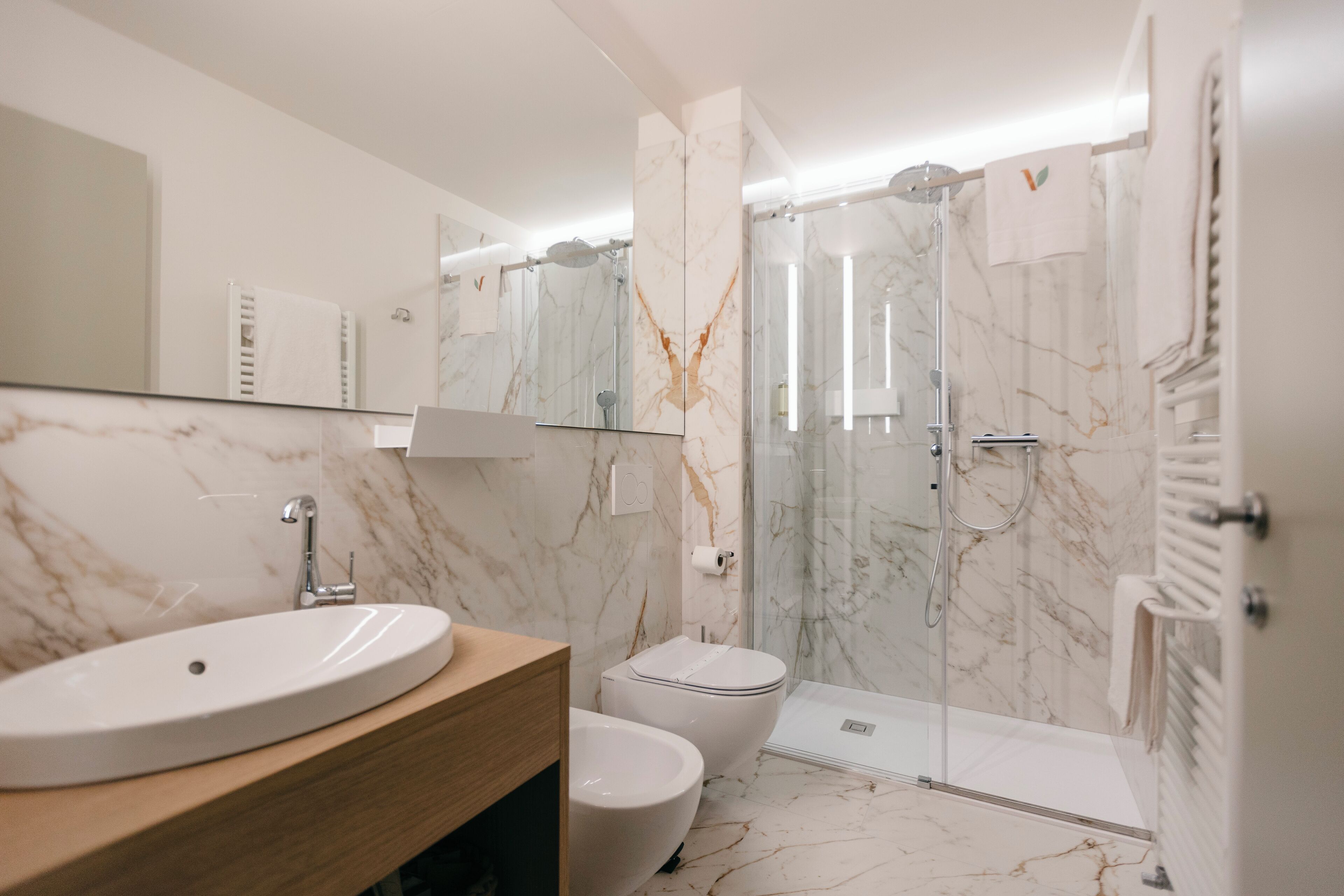Un baño moderno con lavamanos de mármol, inodoro y ducha con mampara de vidrio.