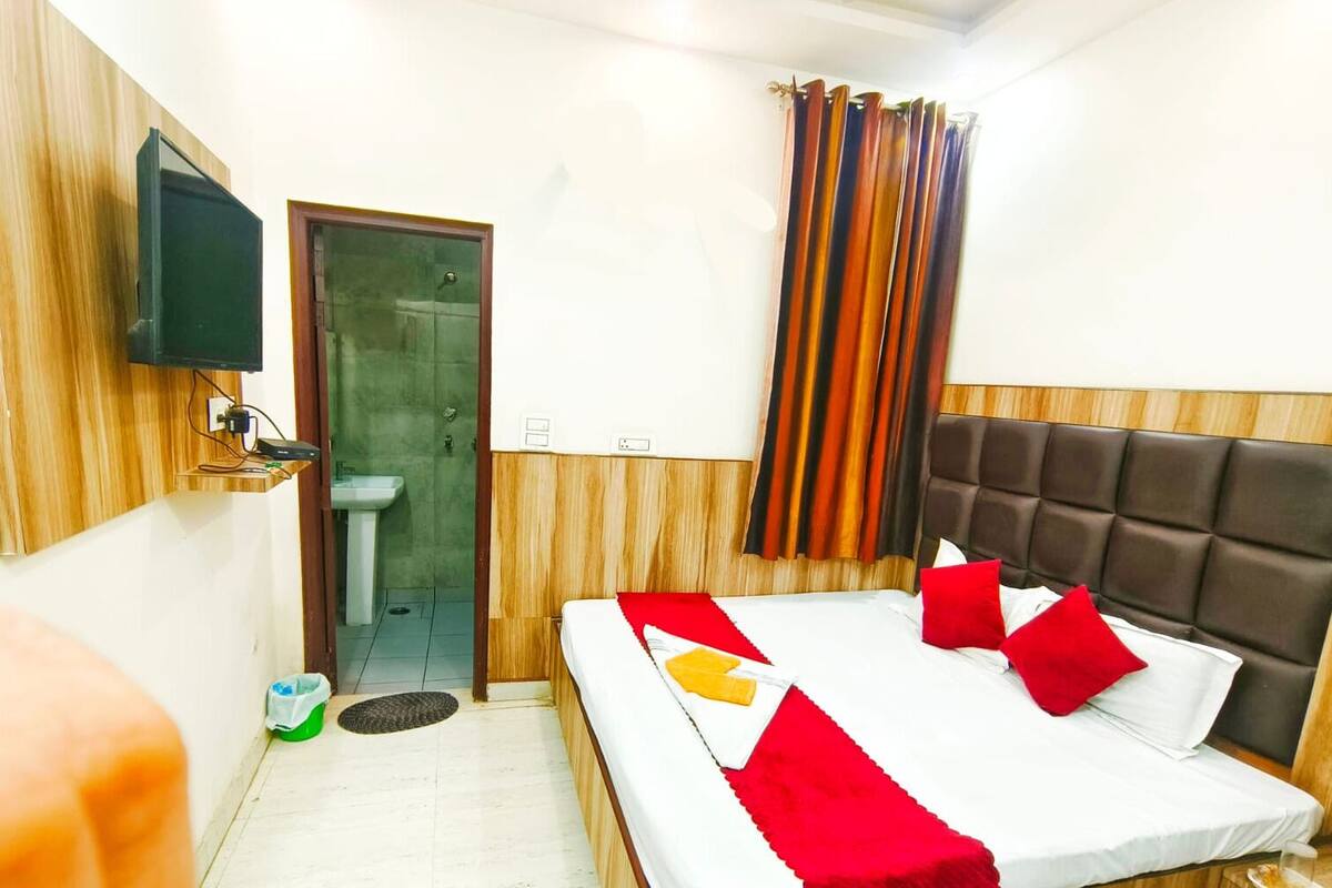 A hotel room with a bed, a television mounted on the wall, a sink, and a window with curtains.
