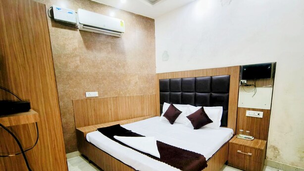 A modern bedroom with a wooden bed frame, a black upholstered headboard, a bedside table, and a built-in TV. - Hotel Silver Star (Panipat)