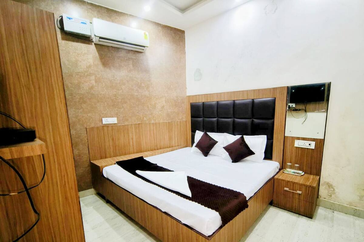 A modern bedroom with a wooden bed frame, a black upholstered headboard, a bedside table, and a built-in TV.