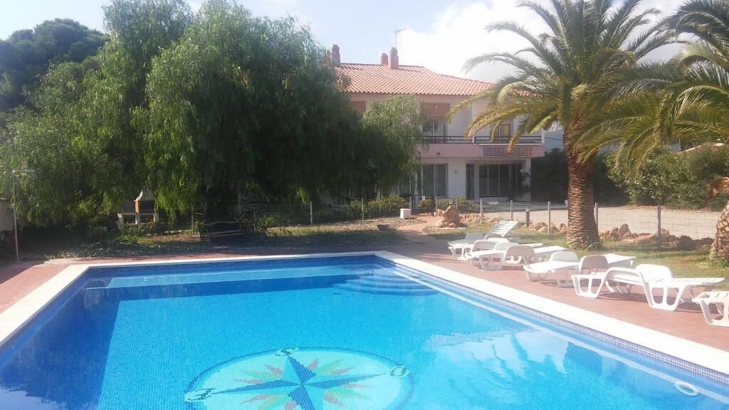 Una piscina con lettini, immersa nel verde e affiancata da un edificio con tetto in tegole rosse.