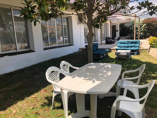 En utomhusplats med sittmöbler, bestående av ett vitt bord och stolar, en blå soffa och en pergola.