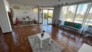 Un'ampia hall dell'hotel con una reception, un divano con un cuscino verde, un tavolino da caffè bianco con piante e una grande finestra che offre vista all'esterno.