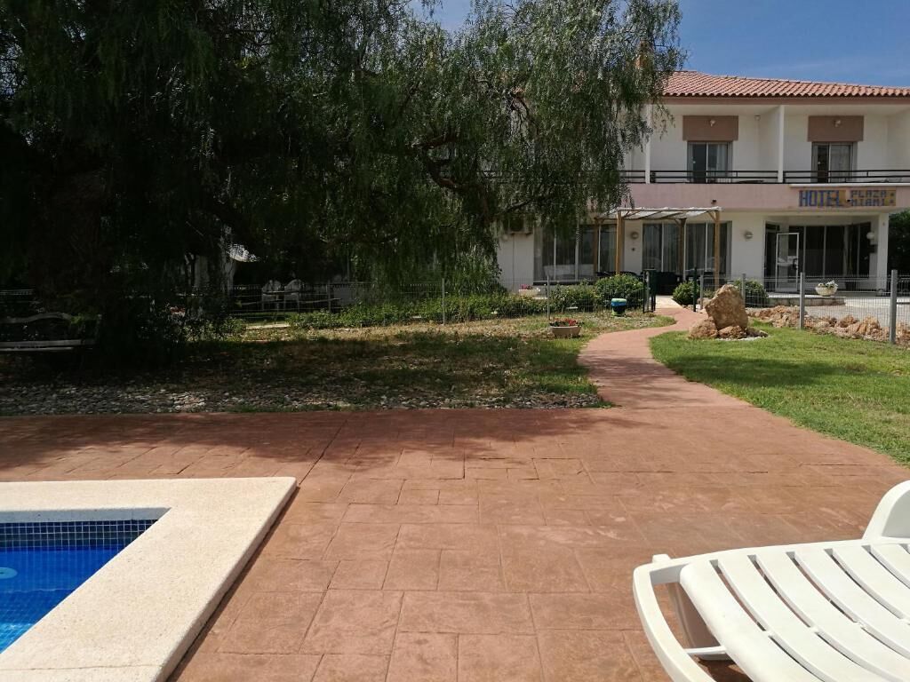 Un hotel con piscina, patio cubierto y jardín con un sendero.