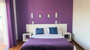 Un dormitorio con una pared morada, una cama con almohadas blancas y azules, y dos mesitas de noche con lámparas.