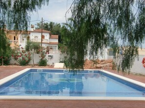 A rectangular swimming pool with clear blue water, surrounded by a brick patio. In the background, there is a white building with a tiled roof and arched windows. - Hotel Plaza Miami Solo adultos (Mont-roig del Camp)