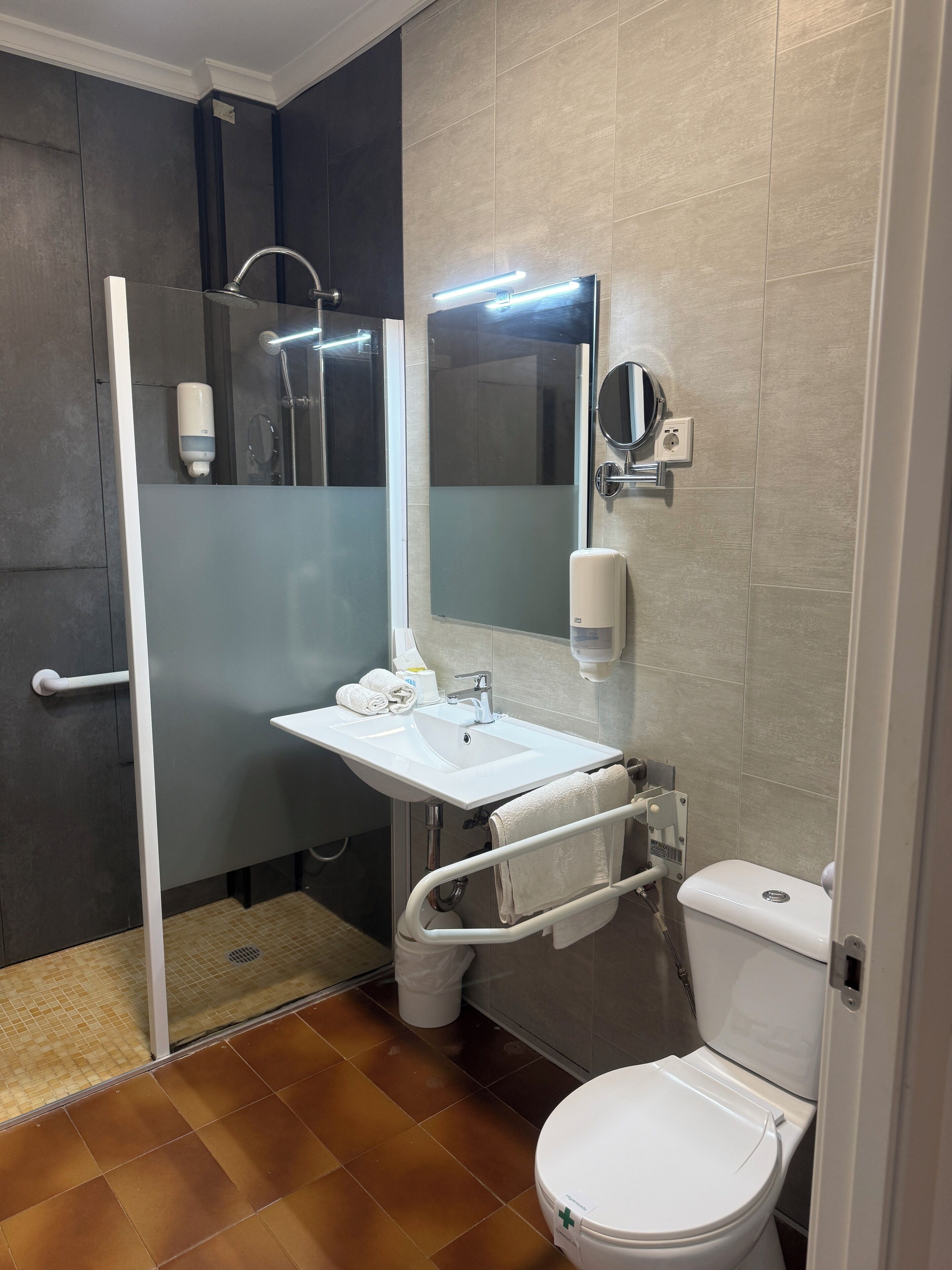 Een moderne badkamer met een douche, een wastafel met spiegel en een toilet.