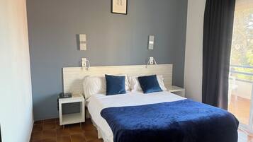 Quarto de hotel com uma cama, mesas de cabeceira brancas, um criado-mudo e uma vista para o exterior.