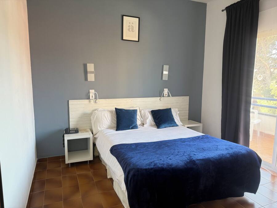 Quarto de hotel com uma cama, mesas de cabeceira brancas, um criado-mudo e uma vista para o exterior.