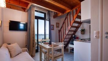 A cozy room with a bed, a dining table with chairs, a TV mounted on the wall, and a staircase leading to an upper level.