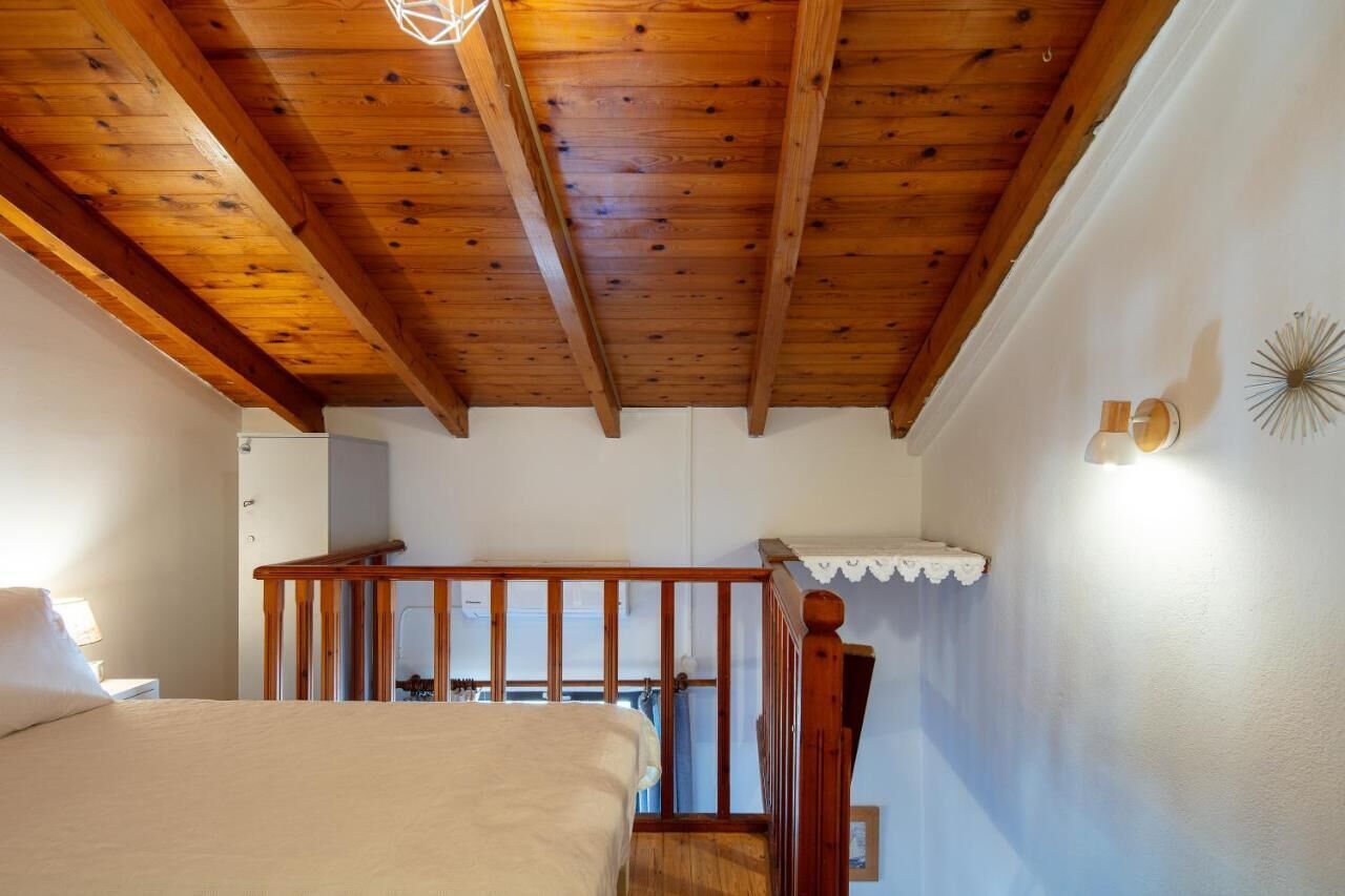 A bedroom with a wooden ceiling, a bed, a nightstand, and a staircase leading to an upper level.