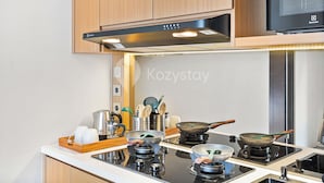 A modern kitchen with wooden cabinets, a black range hood, and a flat-screen TV mounted above the stove. - Pelora Villa by Kozystay - Jimbaran (Jimbaran)