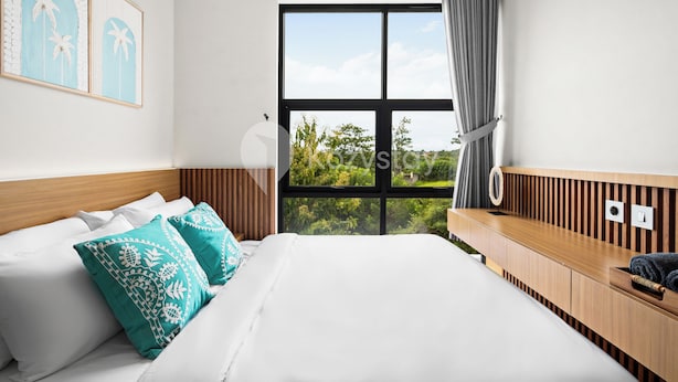 A modern hotel room with a large bed, a wooden console table, a window with a view of greenery, and two wall-mounted artworks. - Pelora Villa by Kozystay - Jimbaran (Jimbaran)