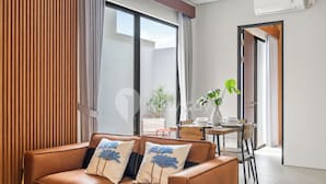 A modern living room with a brown leather sofa, two decorative pillows, a small table with a vase, and a dining area with chairs. - Pelora Villa by Kozystay - Jimbaran (Jimbaran)