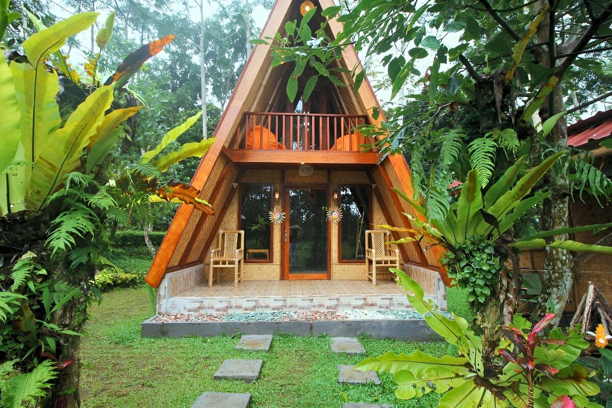 A triangular wooden structure with a balcony, surrounded by lush greenery.