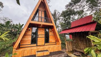 Una casa a forma di A in legno con un balcone, immersa nel verde.