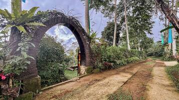 A rustic pathway leading through a lush garden with a large, arched wooden structure.