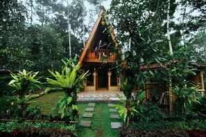 A wooden house with a triangular roof, surrounded by lush greenery and a stone pathway leading to the entrance. - Sanda Eco Cabins by AGATA (Pupuan)