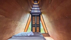 Ein gemütlicher, dreieckiger Raum mit einem Bett in der Mitte, einem Fenster hinten und einer Tür, die nach draußen führt.