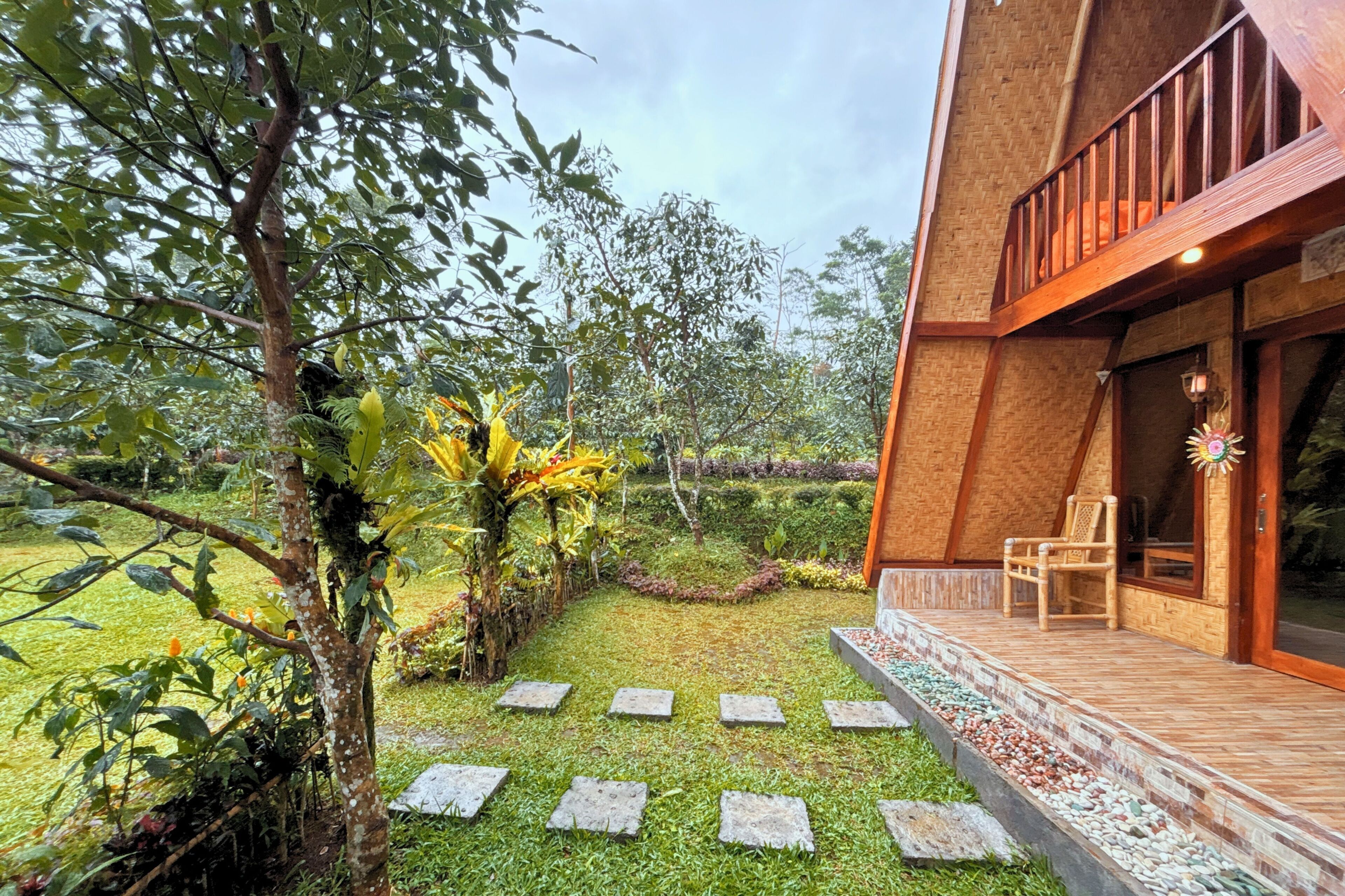 A modern building with a wooden deck, stone pathway, and lush greenery.