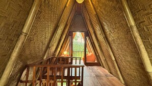 Ein Zimmer mit schrägem Dach, Holzbalken und einem Fenster mit Vorhängen.