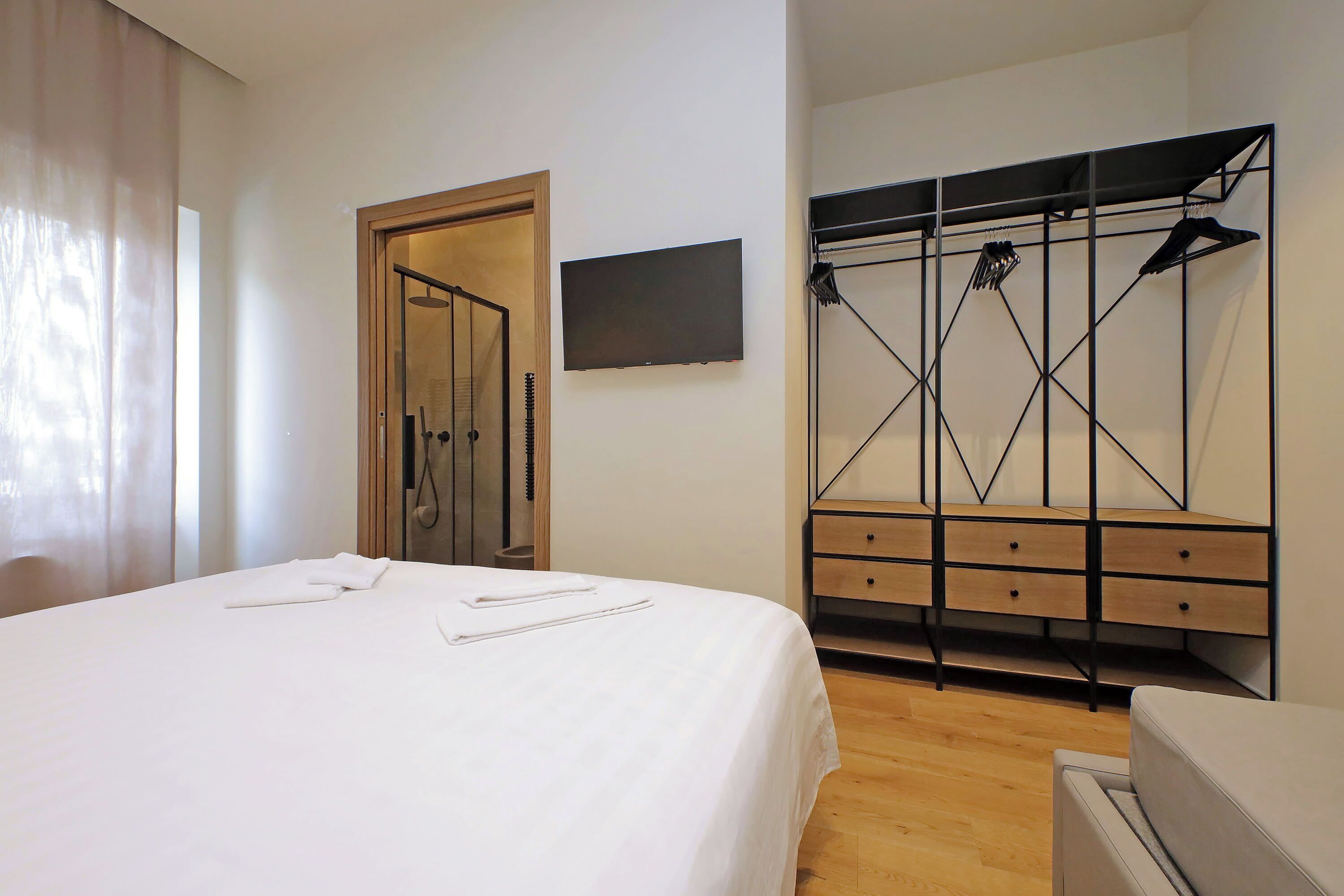 Une chambre d’hôtel comprenant un lit, une armoire en bois, un téléviseur et un espace douche.