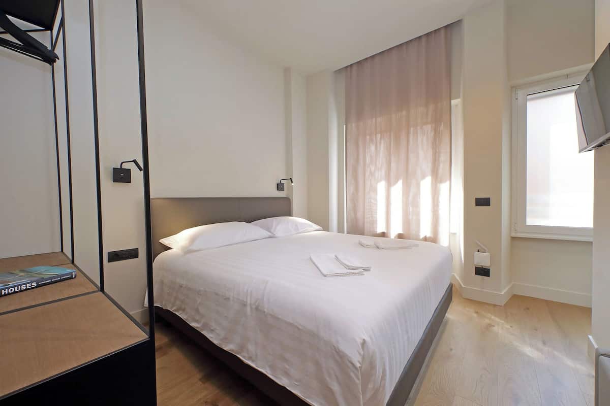 A hotel room with a bed, a bedside table, a TV, and a window with curtains.
