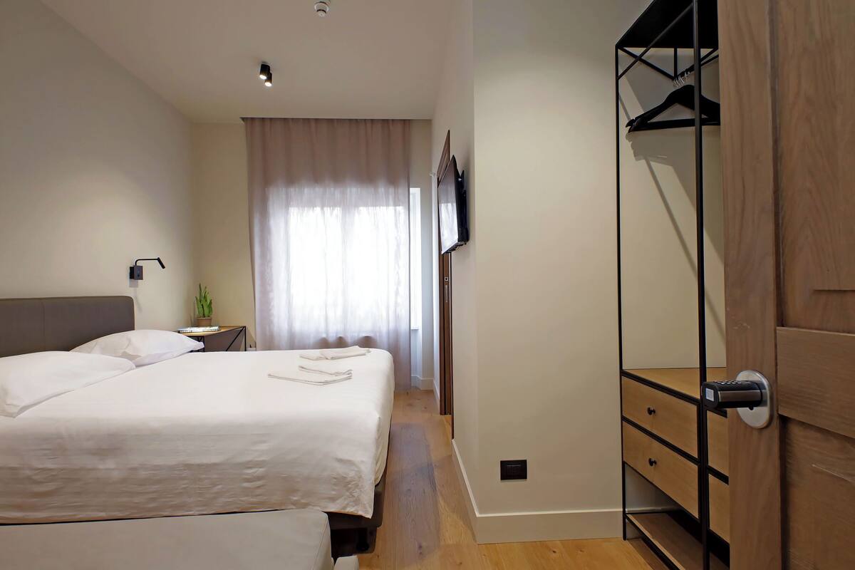 A hotel room with a bed, bedside table, lamp, and a wardrobe with a hanging rack.