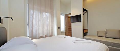 A modern hotel room with a large bed, a sofa, a flat-screen TV, and a desk lamp.