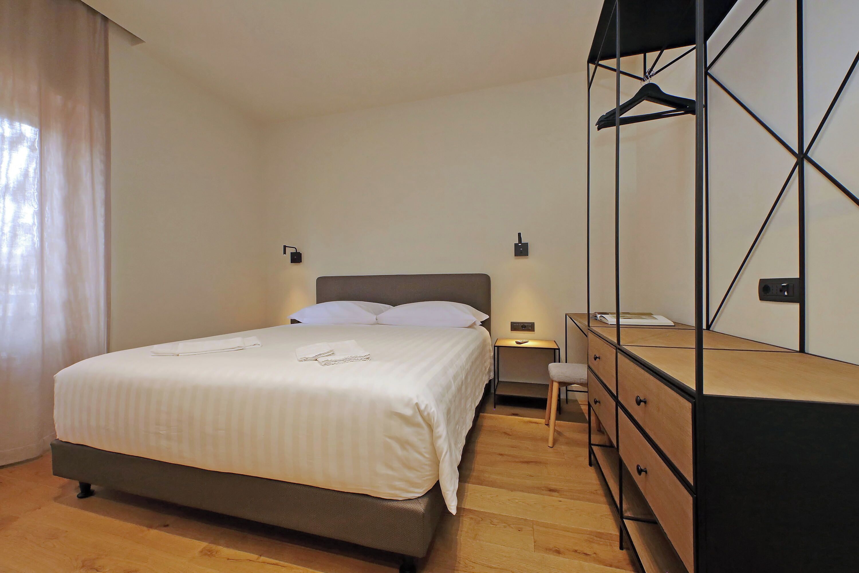 A bedroom with a bed, bedside table, dresser, and a mirror with a hanger.