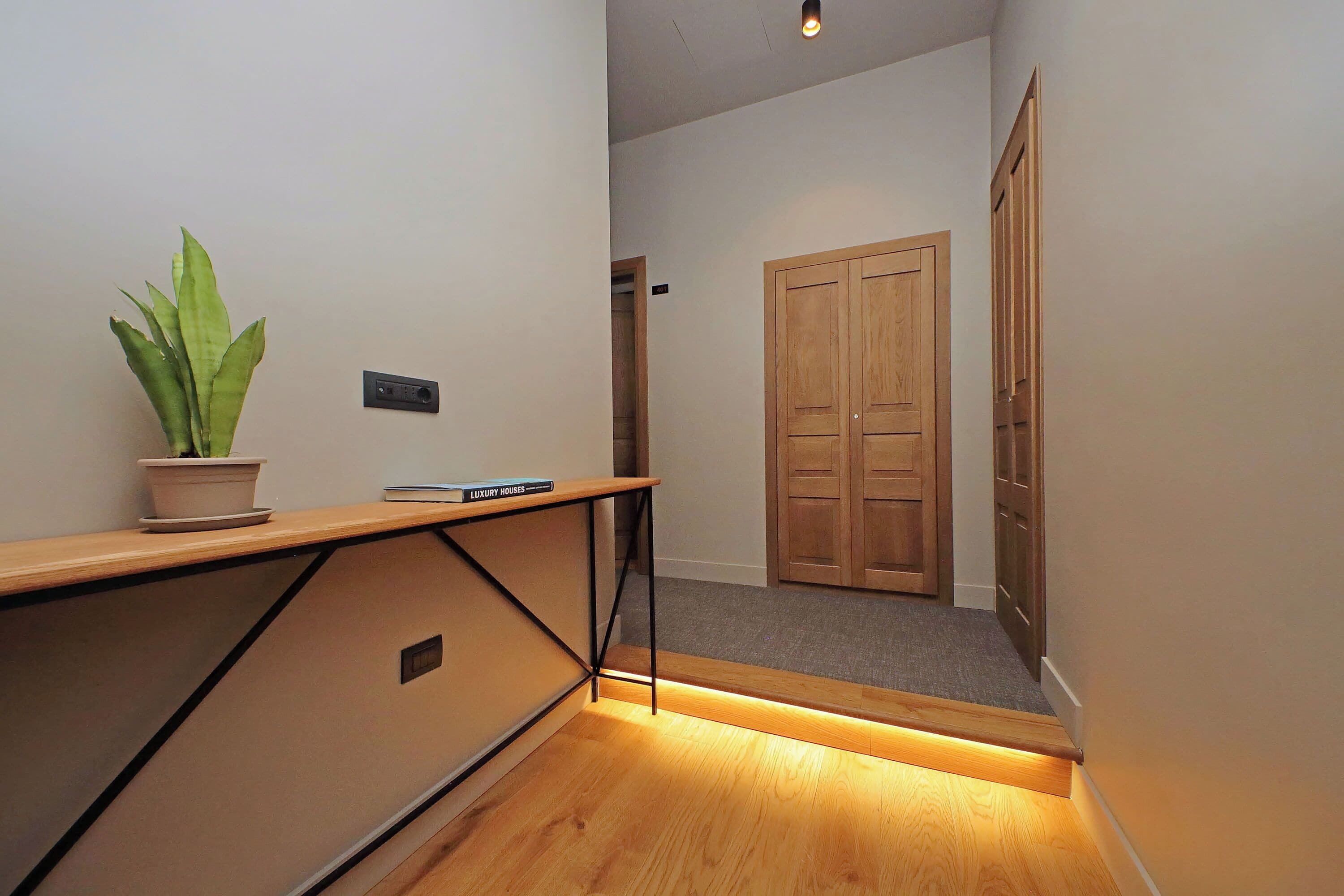 Un pasillo con suelo de madera, una planta en maceta, un libro titulado 'Luxury Houses' y una puerta de madera al final.